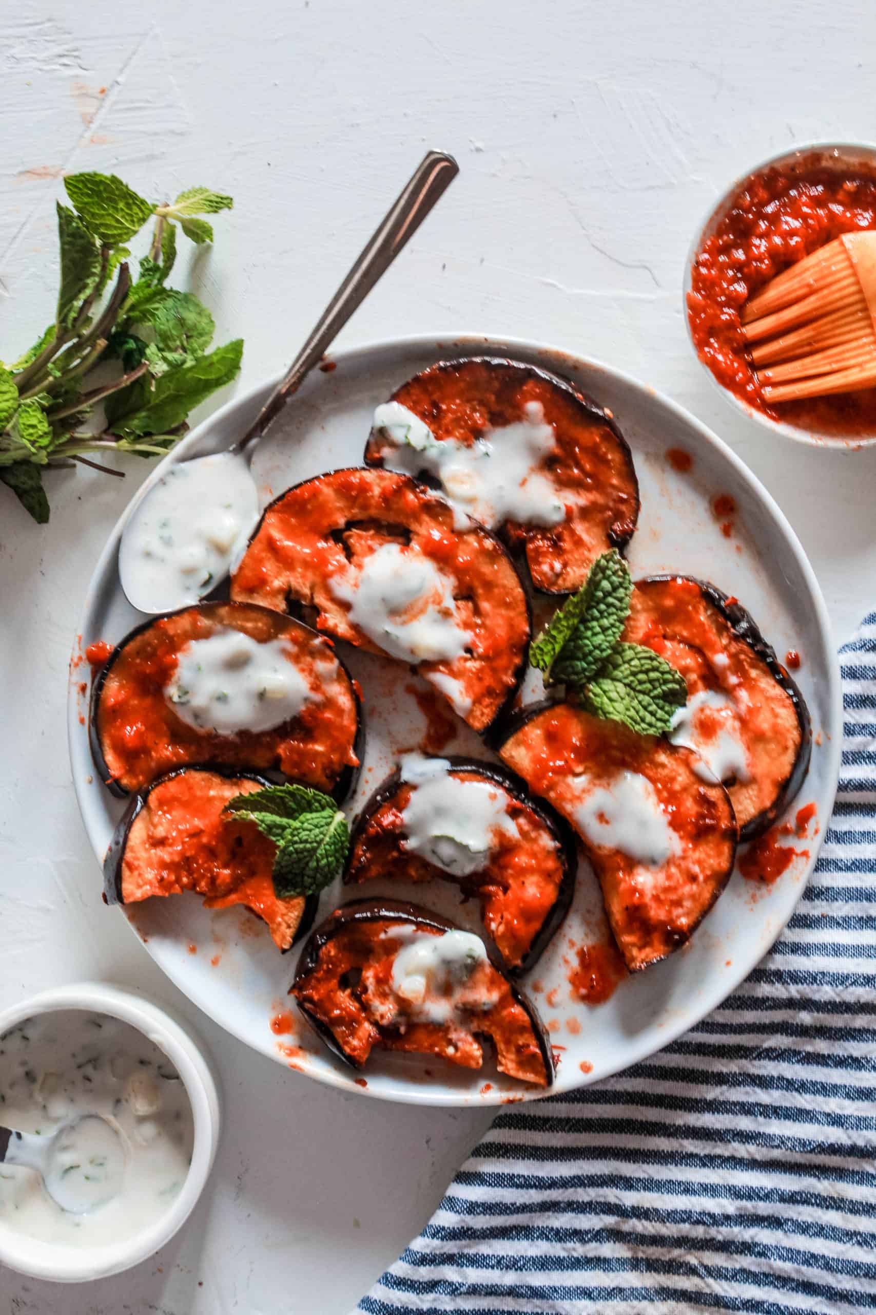 Super simple, healthy stovetop harissa eggplant recipe topped with a delicious mint yogurt sauce. Serve on its own as a side or mix in salads or pasta! #eggplant #harissa