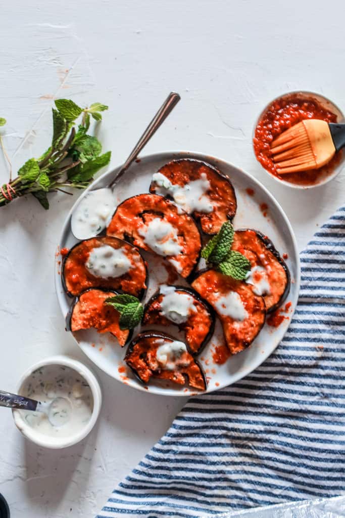 Super simple, healthy stovetop harissa eggplant recipe topped with a delicious mint yogurt sauce. Serve on its own as a side or mix in salads or pasta! #eggplant #harissa