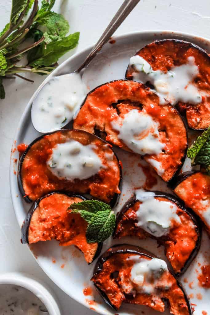 Super simple, healthy stovetop harissa eggplant recipe topped with a delicious mint yogurt sauce. Serve on its own as a side or mix in salads or pasta! #eggplant #harissa